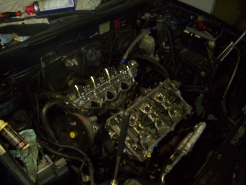 Engine bay with valve covers removed, showing internal engine components. Tools and cleaning supplies are visible