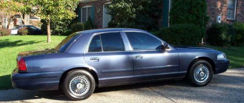 1998 Ford Crown Victoria - Side view of a blue 1998 Ford Crown Victoria sedan parked in front of a house.
