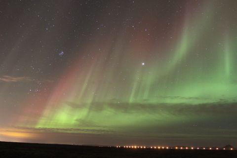 1970 Ford Mustang - The night sky displays a vibrant aurora borealis above a dark landscape dotted with faint lights.