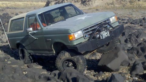 1989 Ford Bronco - A green Ford Bronco navigates a rocky terrain with a custom bumper and winch.