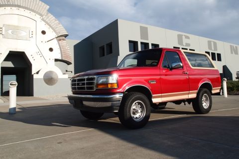 1994 Ford Bronco - This red Ford Bronco is parked in front of a modern building and a unique architectural element.