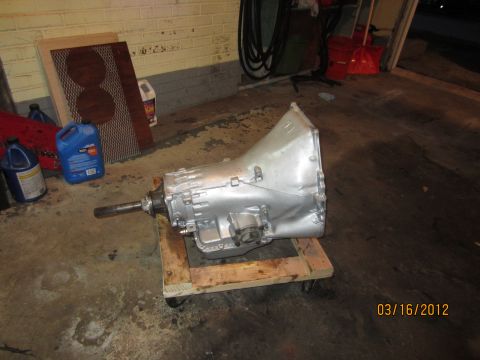 1979 Ford Bronco - A silver automatic transmission sits on a wooden dolly in a garage setting, with various automotive fluids and a speaker grille nearby.