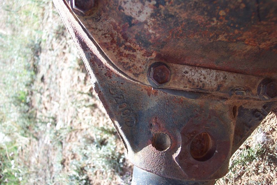 Rusty differential housing with hex bolts and stamped casting numbers, shot outdoors on grass