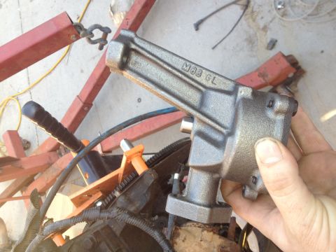 1992 Ford Bronco - A gray metal engine part, possibly from a motor rebuild, is held over an engine block.