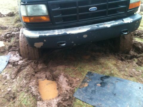 1994 Ford F-150 - A 1994 Ford F-150 is stuck in the mud, with its front tires partially submerged.
