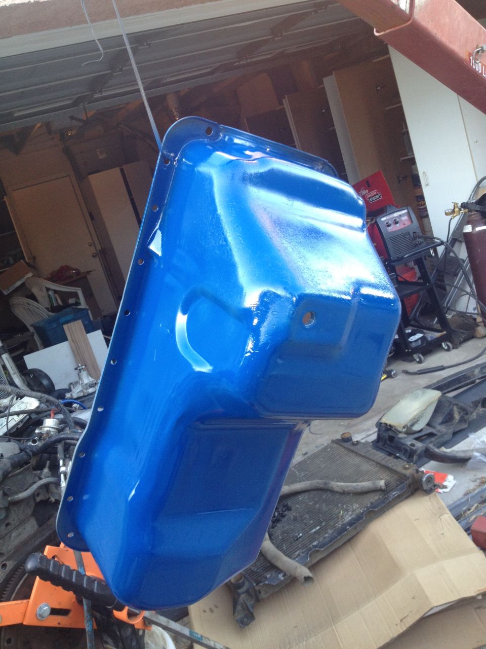 Blue painted oil pan hanging from a hoist in a garage