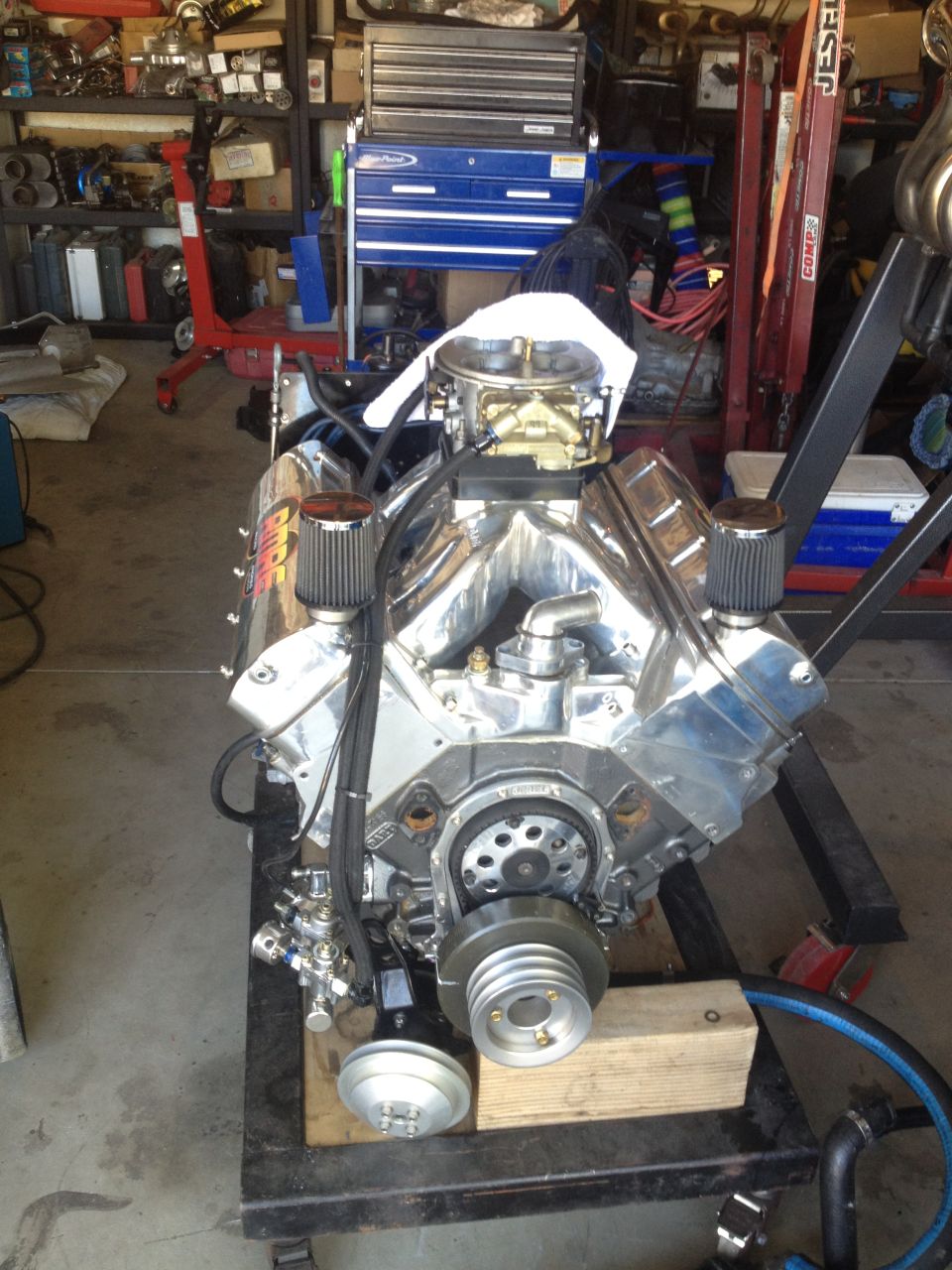 V8 engine on stand, chrome valve covers, dual air filters, carburetor, pulley system visible
