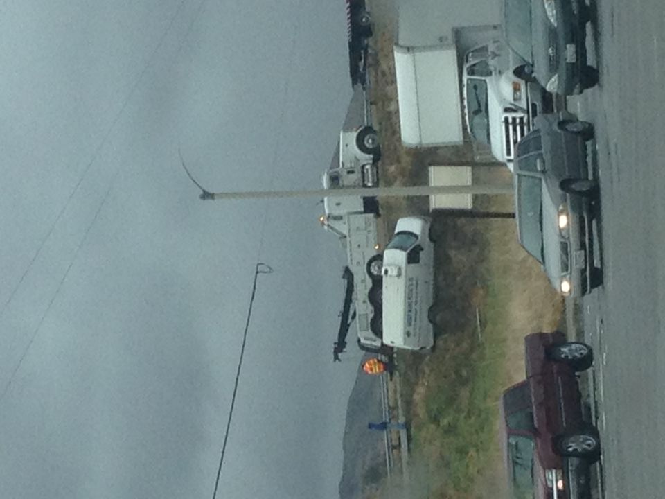 tow truck with a crane arm extended, parked next to other vehicles on a cloudy day