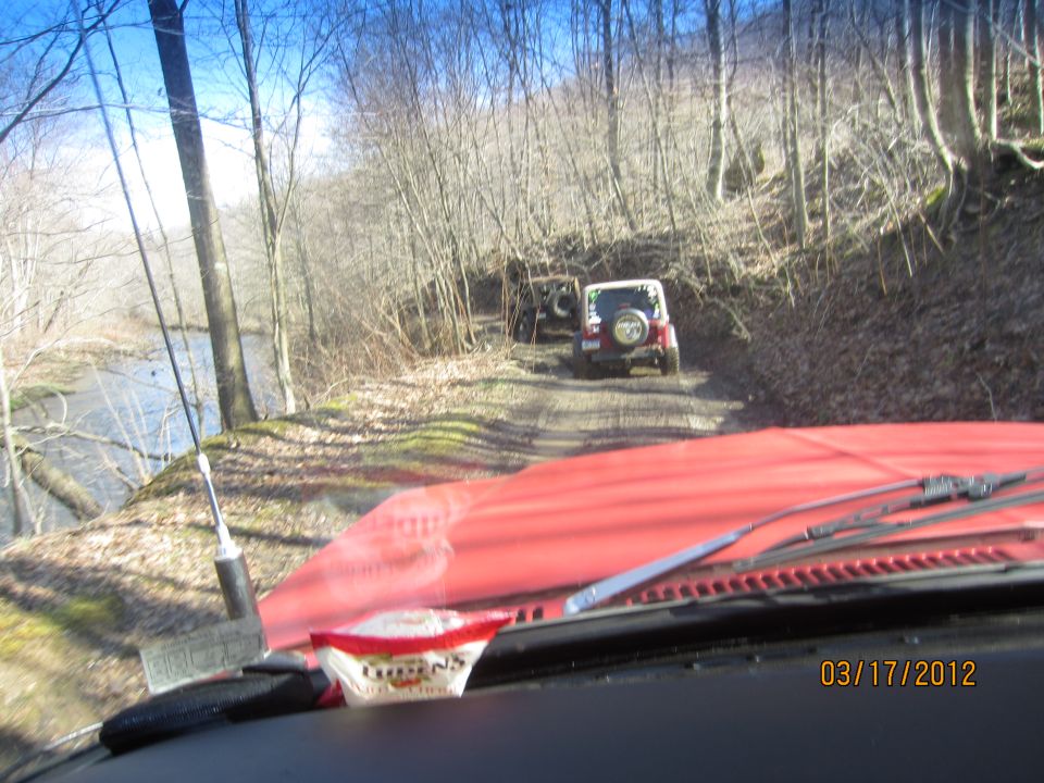 Interior view of red vehicle, two Jeeps on dirt road by river in woods