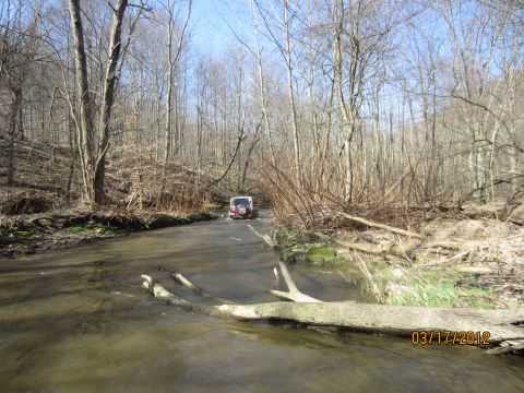 1979 Ford Bronco - A red SUV navigates a shallow creek bed surrounded by bare trees, with a date stamp indicating March 17, 2012.