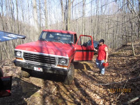 1979 Ford Bronco - A man stands by the open door of a red pickup truck on a wooded trail, with another vehicle in the background.