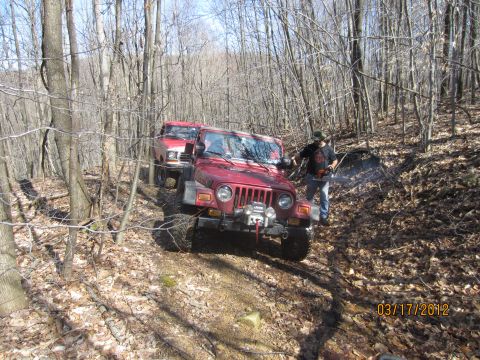 1979 Ford Bronco - Two off-road vehicles navigate a wooded trail on a sunny day.
