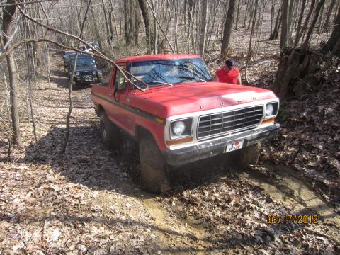 1979 Ford Bronco - This red SUV is navigating a muddy path through a wooded area with another vehicle following.