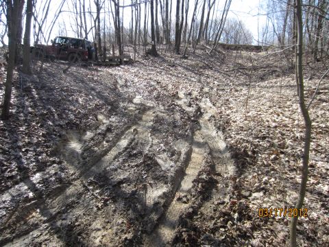 1979 Ford Bronco - A red SUV pulls a trailer through a wooded area with muddy tracks visible.