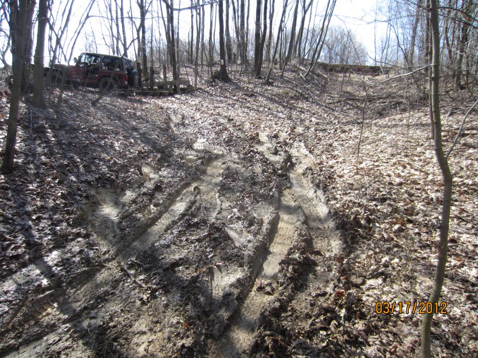 Red SUV towing a trailer on a muddy, leaf-covered forest trail