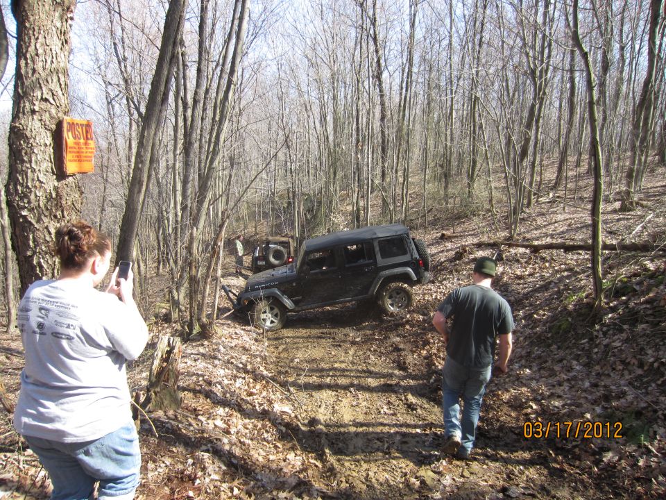 Jeep Wrangler driving on a muddy trail in woods. People watching