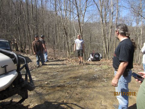 1979 Ford Bronco - Off-road vehicles and people gathered in a wooded area, with one vehicle overturned on the ground.