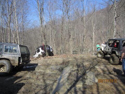 1979 Ford Bronco - Several off-road vehicles navigate a challenging muddy trail in a wooded area.