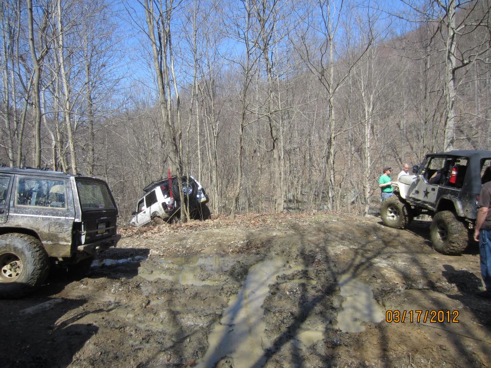 Jeep stuck in mud, another Jeep and SUV nearby in wooded area
