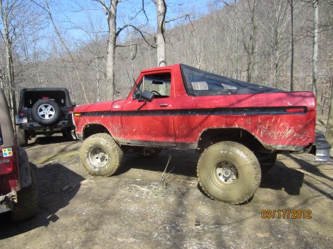 1979 Ford Bronco - A red 1978 Ford Bronco is parked on a dirt path with other off-road vehicles.