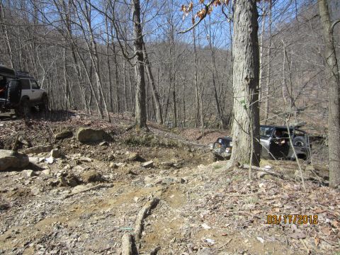 1979 Ford Bronco - Multiple off-road vehicles traverse a challenging, rocky path through a dense forest.