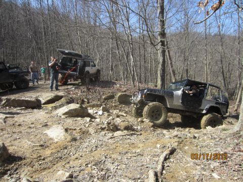 1979 Ford Bronco - Off-road vehicles traverse a challenging, rocky path through a dense forest.