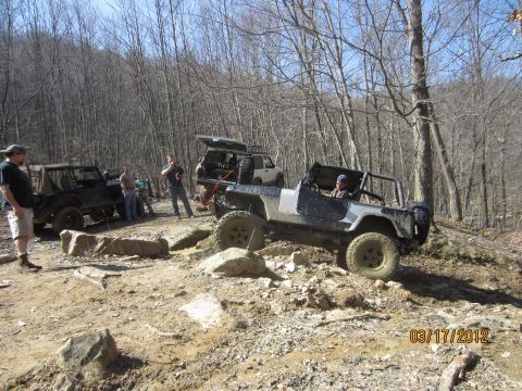 1979 Ford Bronco - Off-road vehicles tackle a challenging rocky path in a wooded area.