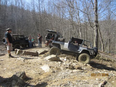 1979 Ford Bronco - Several off-road vehicles are seen traversing a challenging, rocky terrain in a wooded area.
