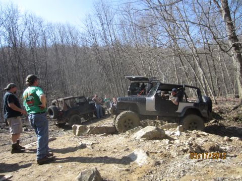 1979 Ford Bronco - Off-road enthusiasts gather to watch vehicles tackle a challenging rocky terrain on a wooded trail.