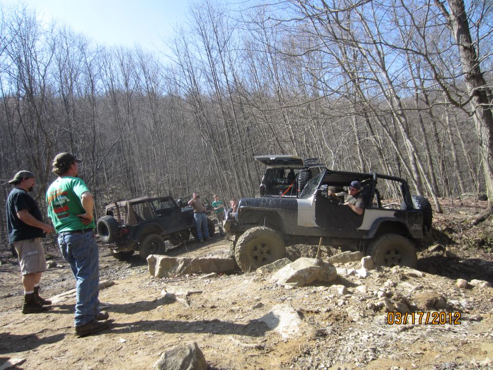 Two off-road vehicles navigate a rocky trail with people watching