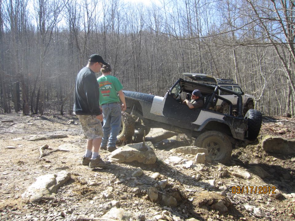 Jeep on rocky trail with two people watching. Another SUV is behind it