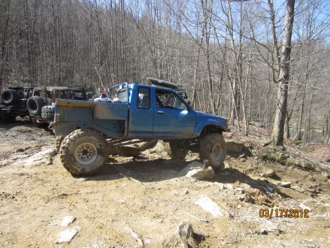 1979 Ford Bronco - Modified blue pickup truck tackles a challenging off-road course with other vehicles present.
