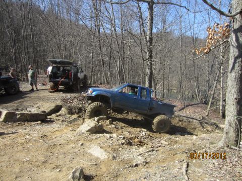 1979 Ford Bronco - Off-road vehicles tackle a challenging, wooded terrain with rocky obstacles and dirt paths.