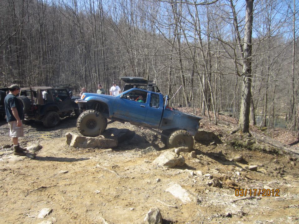 Blue pickup truck with large tires navigating rocks on a dirt trail