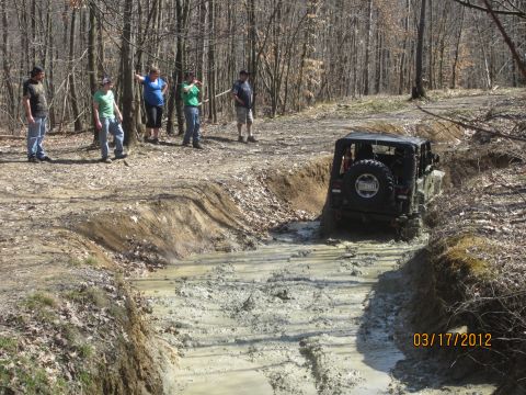 1979 Ford Bronco - Off-roading in a Jeep Wrangler through a challenging mud pit on a wooded trail.