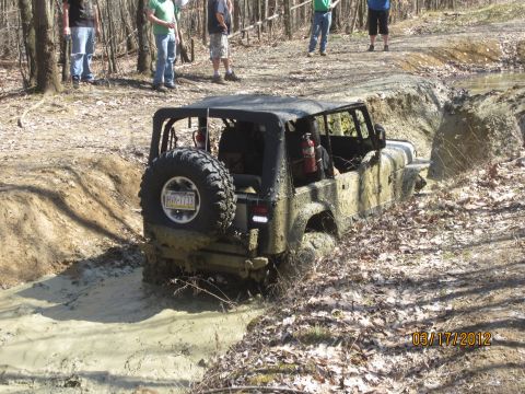 1979 Ford Bronco - A Jeep Wrangler navigates a challenging muddy obstacle course with onlookers present.