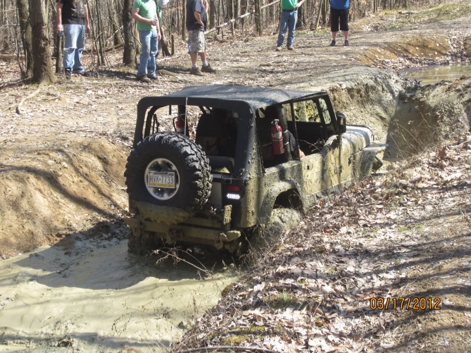 Mud-splattered Jeep Wrangler with spare tire on rear, stuck in a muddy ditch