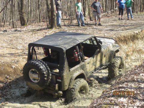 1979 Ford Bronco - A Jeep Wrangler navigates a muddy trail, getting stuck deep in the mud with onlookers observing.