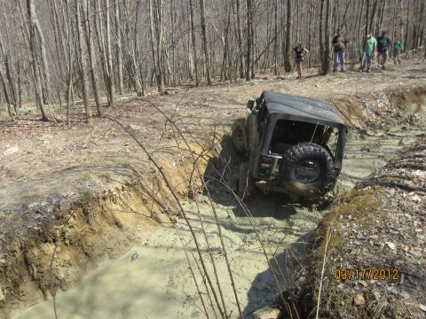 1979 Ford Bronco - A Jeep navigates a challenging muddy obstacle on an off-road trail.