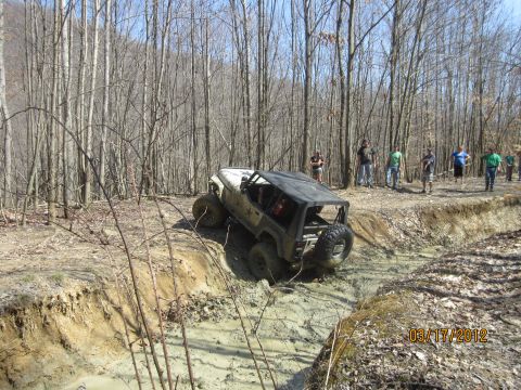 1979 Ford Bronco - A modified off-road vehicle tackles a challenging muddy terrain in a wooded area.