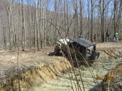 1979 Ford Bronco - An off-road vehicle struggles through a muddy obstacle course in a wooded area.