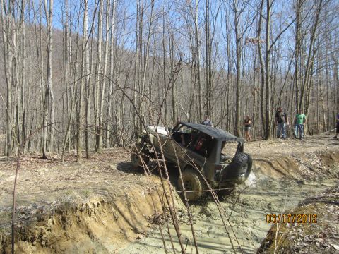 1979 Ford Bronco - Off-road vehicle navigating a challenging muddy terrain in a wooded area.