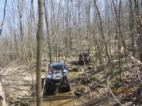 1979 Ford Bronco - Off-road vehicles traverse a water-filled, rocky trail surrounded by bare trees.