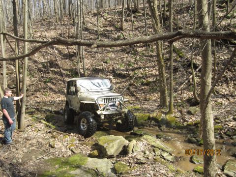 1979 Ford Bronco - A Jeep navigates a wooded trail with a stream and rocks. The date 03/17/2012 is visible.