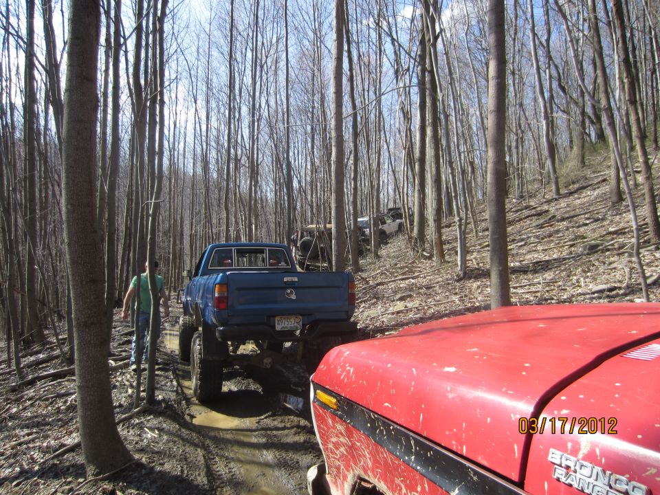 Red vehicle hood in foreground, blue pickup truck and other off-road vehicles on muddy forest trail. Date stamp 03/17/2012