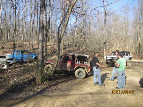 1979 Ford Bronco - Several off-road vehicles are gathered on a muddy trail surrounded by trees.