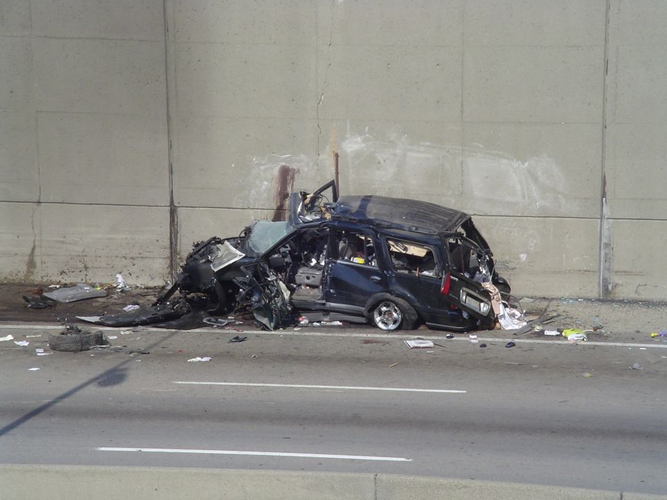 Wrecked dark blue SUV, front passenger side damaged, on highway shoulder
