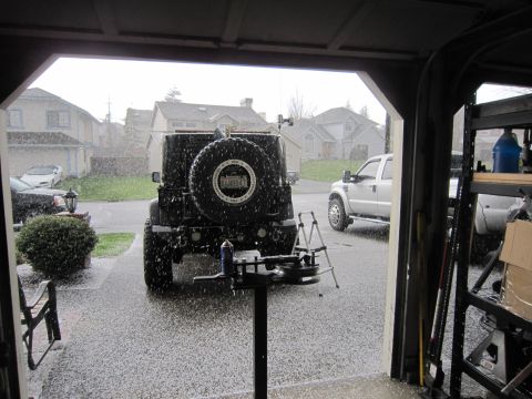 2008 Jeep Wrangler - Rear view of a Jeep Wrangler with a spare tire, while hail falls outside a garage.