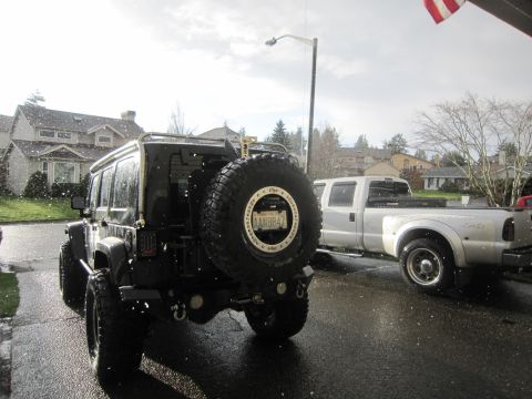2008 Jeep Wrangler - A black Jeep Wrangler is parked on a wet street next to a white pickup truck, with snow falling.