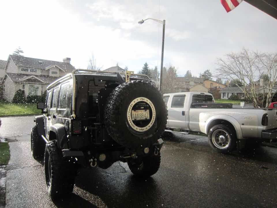 Black Jeep Wrangler with spare tire on back, parked next to a white pickup truck